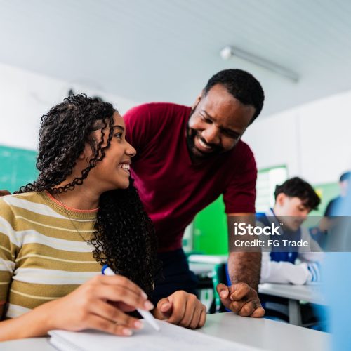 Teacher assisting teenager student during class in classroom